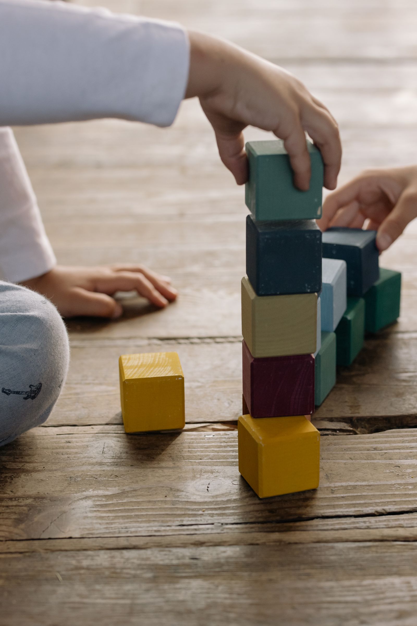 Mãos de uma criança construindo uma estrutura com blocos coloridos