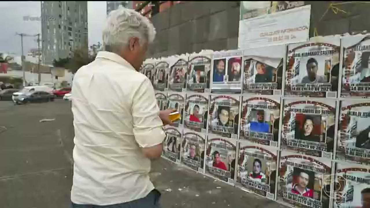 Caco Barcellos observa um muro coberto por cartazes de pessoas desaparecidas